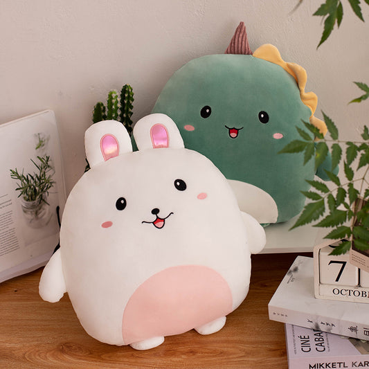 Two cute plush toys, one white bunny and one green dino, on a wooden surface with plants in the background.