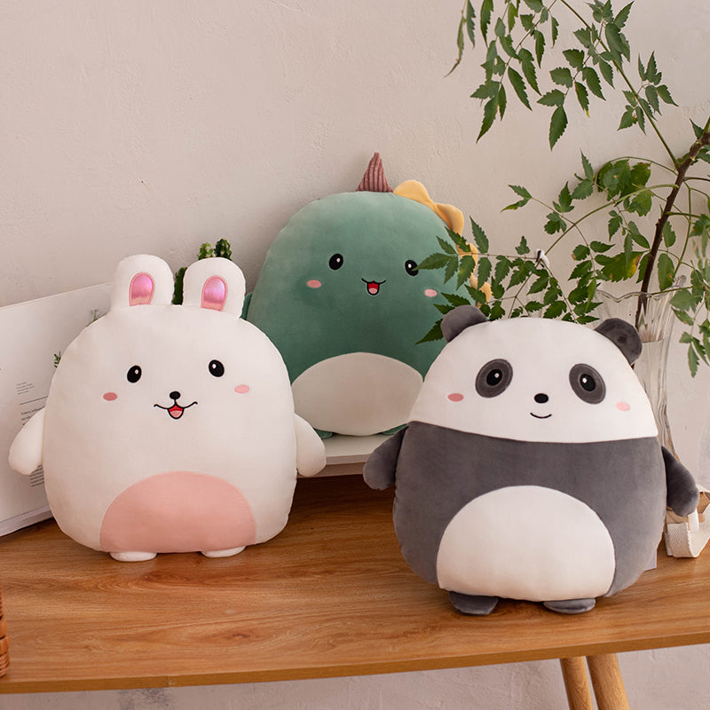 Three cute plush toys, bunny, dino and panda on a wooden surface with a plant in the background