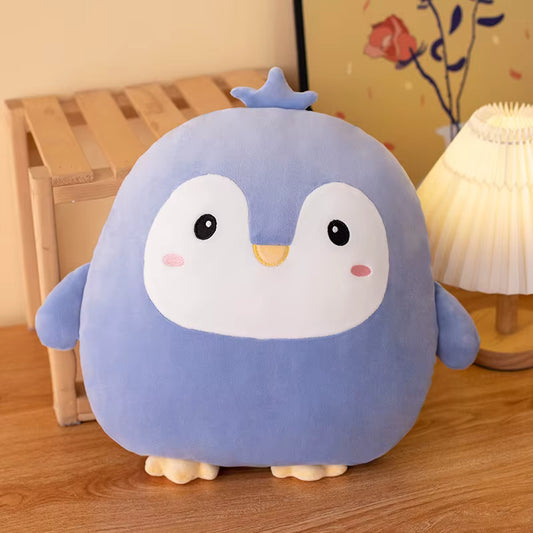 Cute blue plush penguin toy on a wooden floor with a lamp and decorative items in the background.